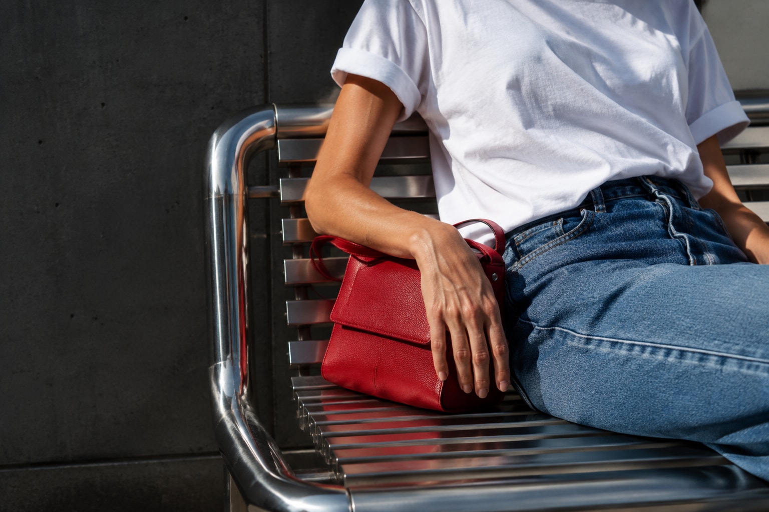 Denim, red leather bag and afternoon light on a city bench